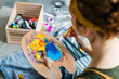 © golubovy - Artist essential tools. Closeup back view of lady using wooden palette and paintbrush to mix paint.