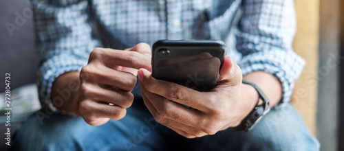 Fotomural Young casual Businessman holding and using smartphone for sms messages, hipster man typing touchscreen cell phone in the cafe