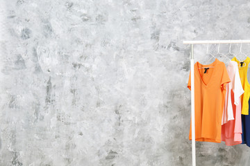 Poster - Women's hip clothing store interior concept. Row of different colorful female clothes hanging on rack in hipster fashion show room in shopping mall. Grunged concrete wall background. Copy space.