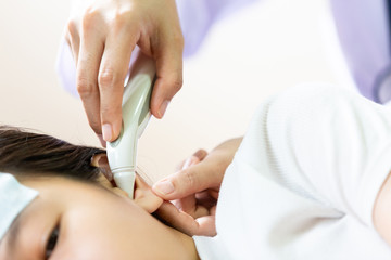 Closeup of hand doctor or nurse checking child patient temperature in the ear using digital thermometer,asian little girl having fever using cold gel placed on her forehead to relief fever,headache 