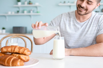 Sticker - Handsome man pouring tasty milk from bottle into glass in kitchen at home