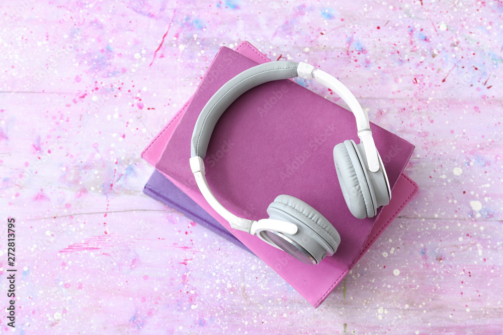 Books and modern headphones on color background. Concept of audiobook