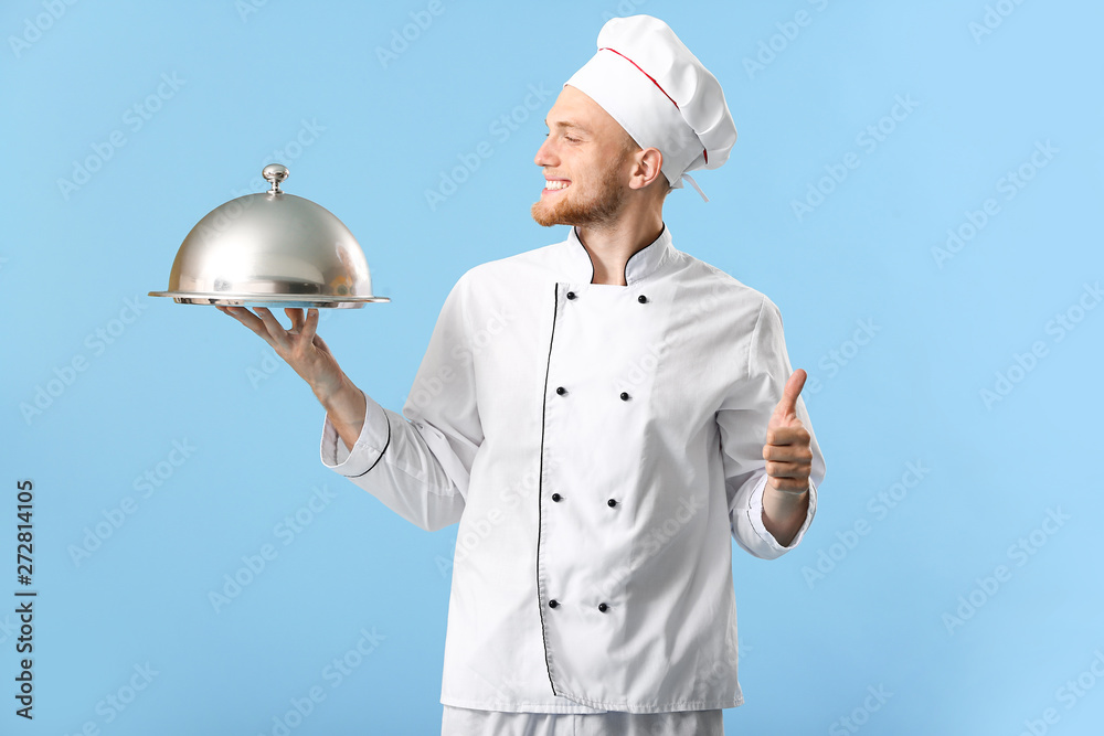 Handsome male chef with tray and cloche on color background