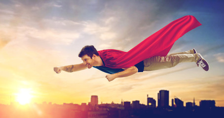 Wall Mural - super power and people concept - happy young man in red superhero cape flying in air over sunset in city of tallinn background