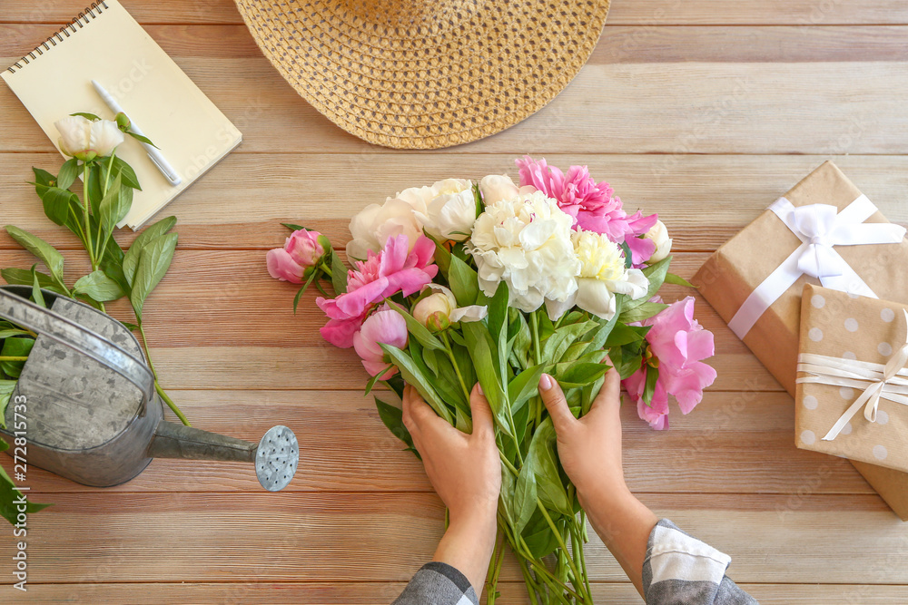 Woman making bouquet of beautiful peonies at table