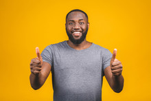 Portrait Of Cheerful, Positive, Handsome Man With Black Skin, Beaming Smile In Casual Showing Thumb Up With Finger To The Camera Isolated On Yellow Background.
