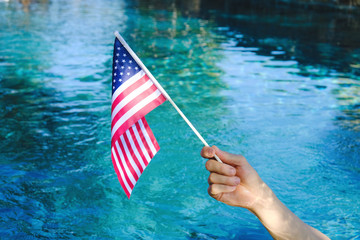 Wall Mural - Hand waving American flag with blue pool water in background.  Fourth of July holiday celebration concept.