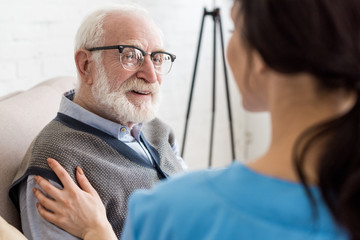 Selective focus of cheerful and grey haired man looking at nurse