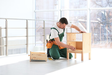 Wall Mural - Handyman in uniform assembling furniture indoors. Professional construction tools