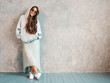 © halayalex - Young beautiful smiling woman looking at camera. Trendy girl in casual summer hoodie and skirt clothes. Funny and positive female posing near gray wall in studio. In sunglasses.