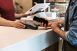 © Drobot Dean - Cropped photo of young man paying debit card in cafe while waiter holding payment terminal