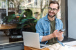 © Drobot Dean - Photo of successful young man holding smartphone while working on laptop in city cafe outdoors