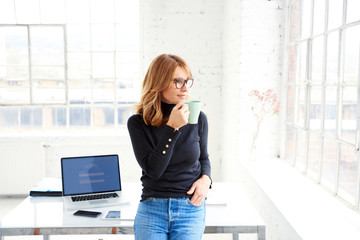 Beautiful businesswoman standing in the office while drinking her coffee