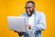 © denis_vermenko - Young surprised african american man standing and using laptop computer isolated over yellow background.