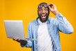 © denis_vermenko - Young surprised african man standing and using laptop computer isolated over yellow background.