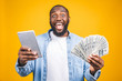 © denis_vermenko - Winner! Young rich african american man in casual t-shirt holding money dollar bills with surprise isolated over yellow wall.