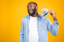 Winner! Young Rich African American Man In Casual T-shirt Holding Money Dollar Bills With Surprise Isolated Over Yellow Wall.