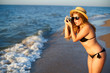 © artiemedvedev - Young authentic woman with vintage retro film camera enjoying tropical beach on summer vacation. Female travel photographer in straw hat taking photos having fun at sea. Real girl unretouched shape.