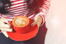 The Woman's Hand Is Holding A Red Cup Of Coffee Latte Art
