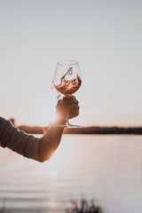 Wall Mural - Glass of rose wine in woman's hand against the sunset sky.