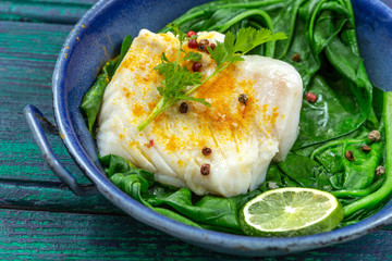 Cod fillet with rice and spinach garnish with curry, in vintage pan on wooden background