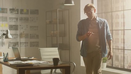 Thoughtful Professional Designer Sits at His Desk and Looks onto City out of His Windows, Contemplating Project Details, Has Idea and Starts Using Laptop. Handsome Professional Working in his Studio
