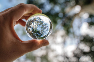 reflection of blue sky, white clouds and trees in a glass ball in holding hand