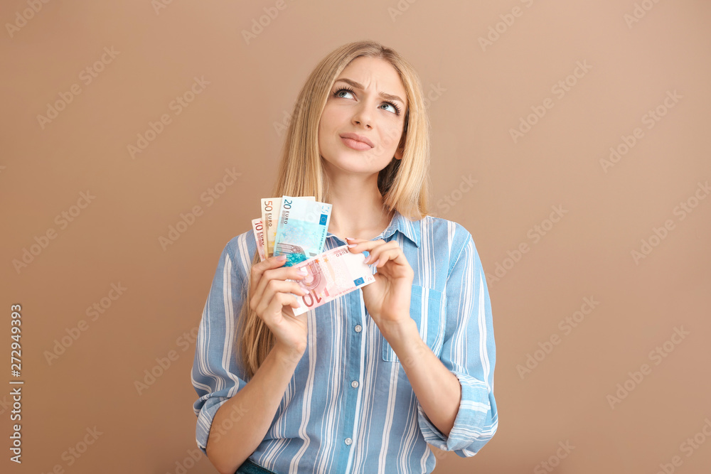 Thoughtful young woman with money on color background