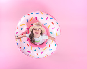 A little child girl lying on a donut inflatable circle. Pink background. Top view. Summer concept.