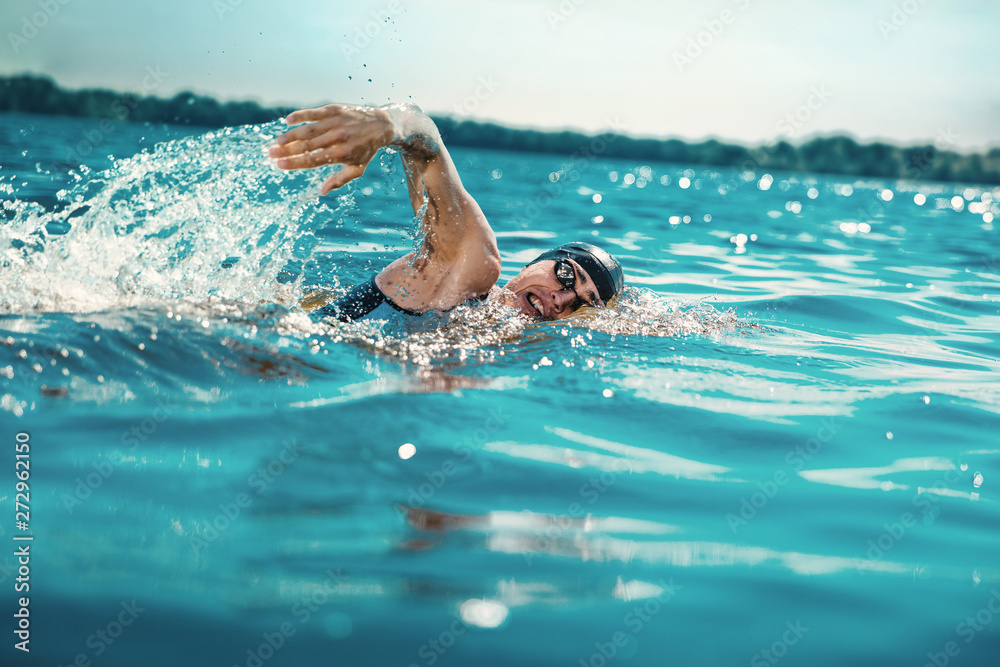Professional triathlete swimming in river's open water. Man wearing swim equipment practicing triathlon on the beach in summer's day. Concept of healthy lifestyle, sport, action, motion and movement. - obrazy, fototapety, plakaty 