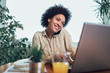© Mediteraneo - Smiling young African female entrepreneur sitting at a desk in her home office working online with a laptop