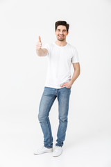 Canvas Print - Excited young man posing isolated over white wall background showing thumbs up gesture.