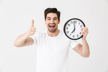 Poster - Shocked excited happy young man posing isolated over white wall background holding clock.