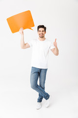 Canvas Print - Emotional excited young man posing isolated over white wall background holding speech bubble.