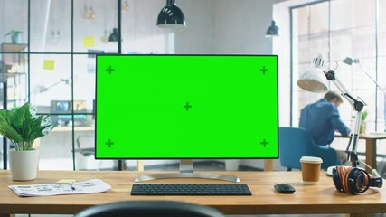 Poster - Wide Green Mock-up Screen Desktop Computer Standing on the Desk in the Modern Creative Office. In the Background High Ceiling Creative Loft for Developers and Designers where Professional Working.