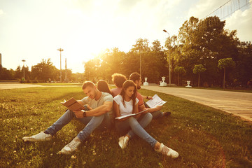 Students study sitting on green grass in a park in summer spring.