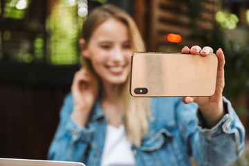 Wall Mural - Happy young pretty blonde woman in cafe using laptop computer and mobile phone take a selfie.