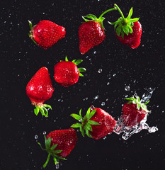 Wall Mural - Bright and juicy strawberries thrown into the air on a black and gray background with chaotic splashes of water