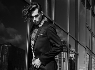 handsome fashion male model dressed in elegant suit posing outdooe. Long haired Metrosexual. Black and white picture.