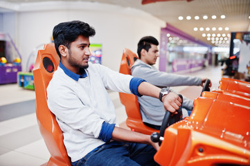 Two asian guys compete on speed rider arcade game racing simulator machine.