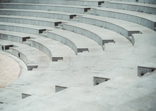 Rows Of Grayish Stony Or Marble Seats And Flights Of Stairs Of A Modern Outdoor Amphitheater With A Pavement Stone On The Stage Down Below