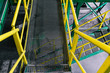 The metal ladder painted in green and yellow colors. Iron ladder in an industrial plant or factory. Metal grating on the floor