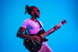 © master1305 - Young african-american musician playing the guitar like a rockstar on blue studio background in neon light. Concept of music, hobby. Joyful attractive guy improvising. Retro colorful portrait.