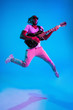© master1305 - Young african-american musician playing the guitar in jump like a rockstar on blue studio background in neon light. Concept of music, hobby. Joyful attractive guy improvising. Retro colorful portrait.