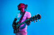 © master1305 - Young african-american musician playing the guitar like a rockstar on blue studio background in neon light. Concept of music, hobby. Joyful attractive guy improvising. Retro colorful portrait.