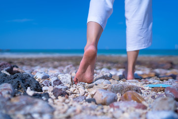 Close up low angle woman barefoot walking on beach with stone ground