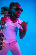 © master1305 - Young african-american musician playing the guitar like a rockstar on blue studio background in neon light. Concept of music, hobby. Joyful attractive guy improvising. Retro colorful portrait.