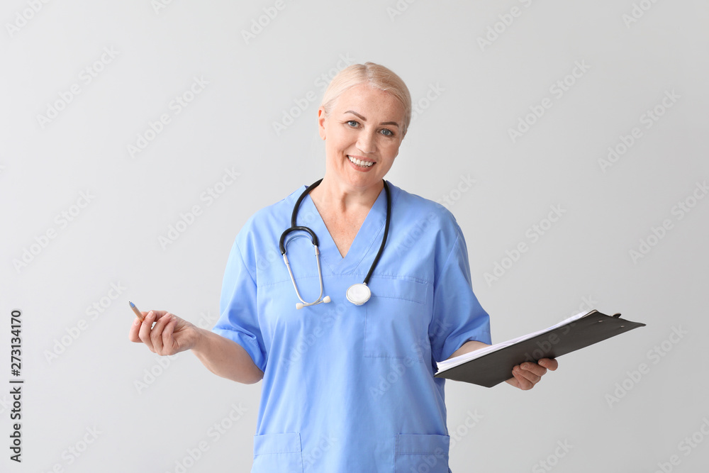 Mature medical assistant with clipboard on grey background