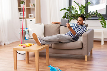 Sticker - people, housework and housekeeping concept - indian man in headphones listening to music on tablet computer after home cleaning