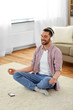 © Syda Productions - mindfulness, meditation and relaxation concept - man in wireless headphones listening to relaxing music on smartphone and meditating in lotus pose at home